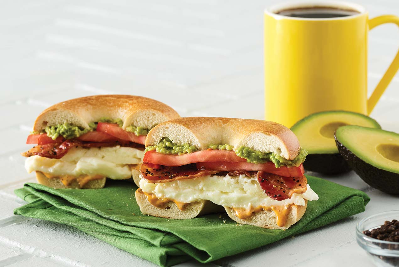 avocado breakfast bagel sandwich cut in half with mug of coffee